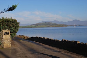 A coastal road leading to Seapoint House with a stone sign, a stone wall, and a view of the sea and distant hills. - Seapoint House (Westport)