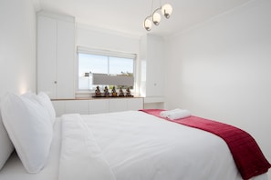 A hotel room with a large bed, white walls, a window with a view, and a red throw blanket. - Bendennis 302 (Cape Town)