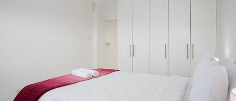 A hotel room with a neatly made bed, white walls, and a large wardrobe.