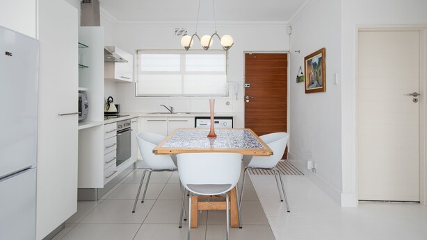 A modern kitchen with white cabinets, a wooden dining table, and a pendant light. - Bendennis 302 (Cape Town)