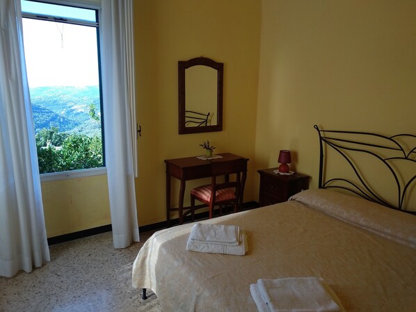 Un dormitorio con una cama, una mesita de noche, una silla, un escritorio, un espejo y una ventana con cortinas.