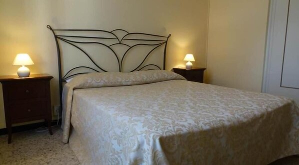 Una cama bien hecha con una colcha estampada, dos mesitas de noche con lámparas y un cabecero sencillo.