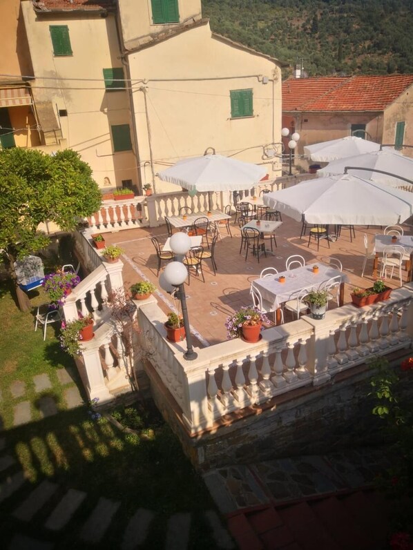 Un patio al aire libre con mesas y sillas, rodeado de plantas en macetas y sombrillas.