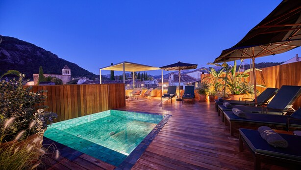 A wooden deck with a swimming pool, lounge chairs, and umbrellas. - Mon Boutique Hotel (Pollenca)