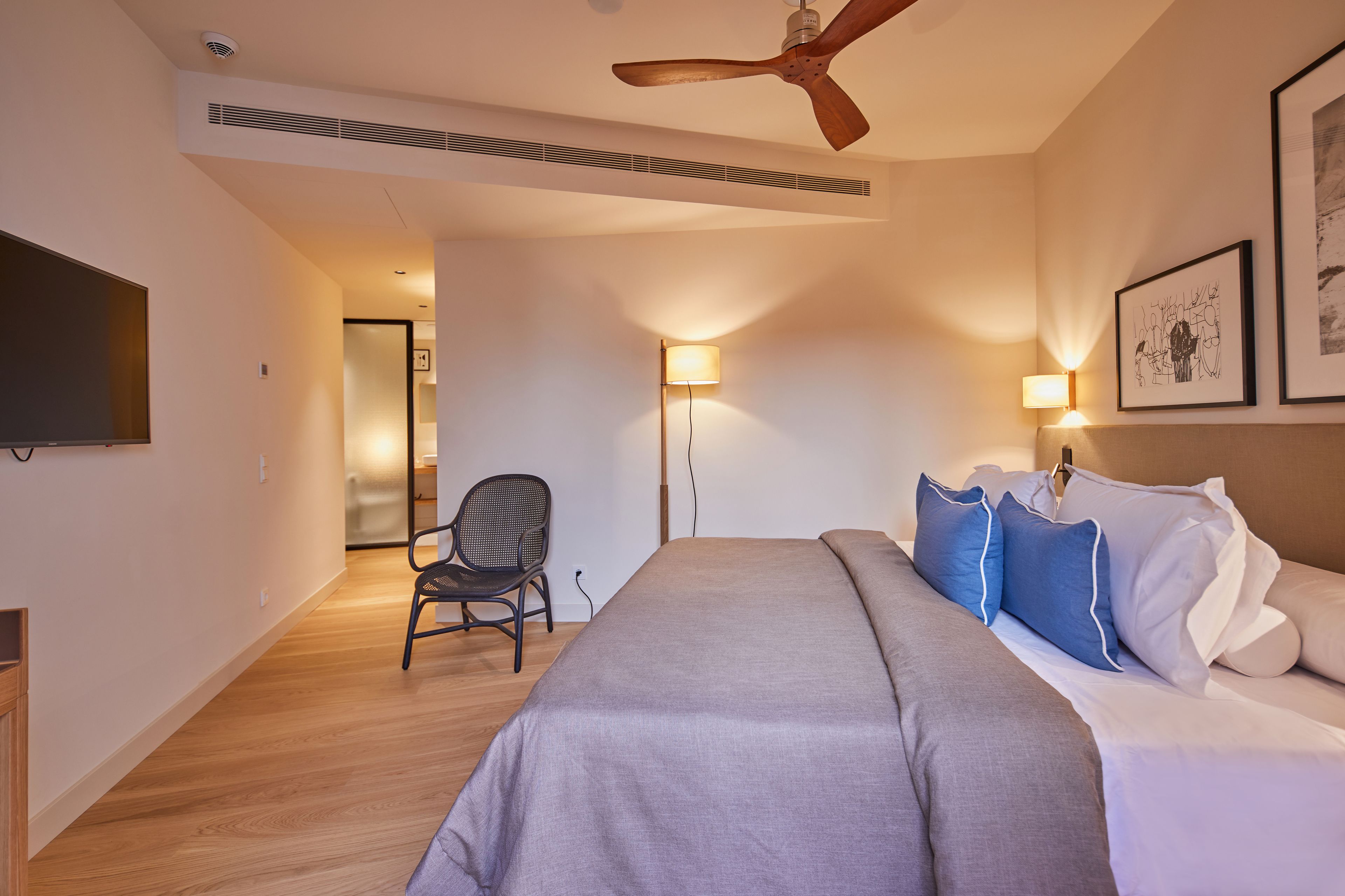 Una habitación de hotel moderna con una cama grande, un ventilador de techo, un televisor de pantalla plana y una silla.