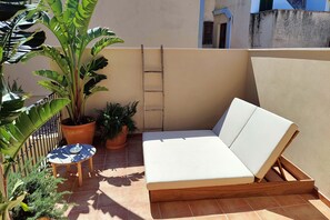 A small outdoor seating area with a white cushioned bench, a small round table, and potted plants. - Mon Boutique Hotel (Pollenca)
