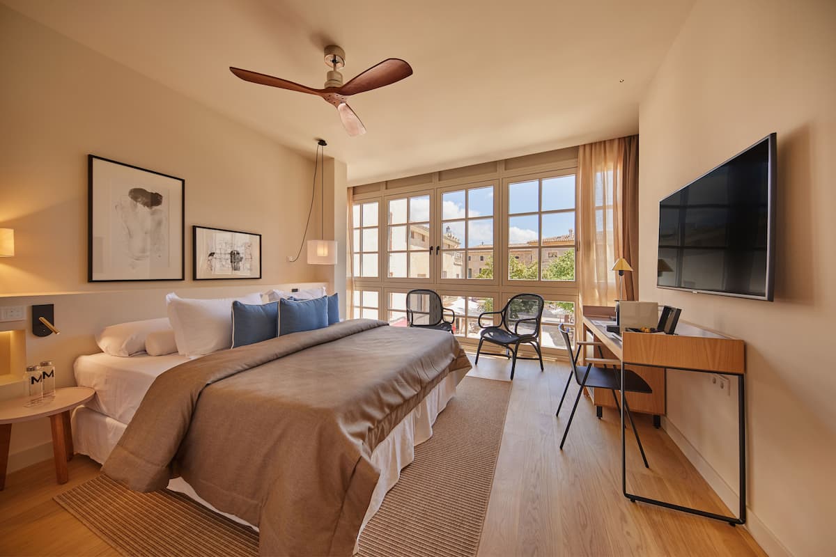 A hotel room with a bed, desk, chair, TV, and large windows.