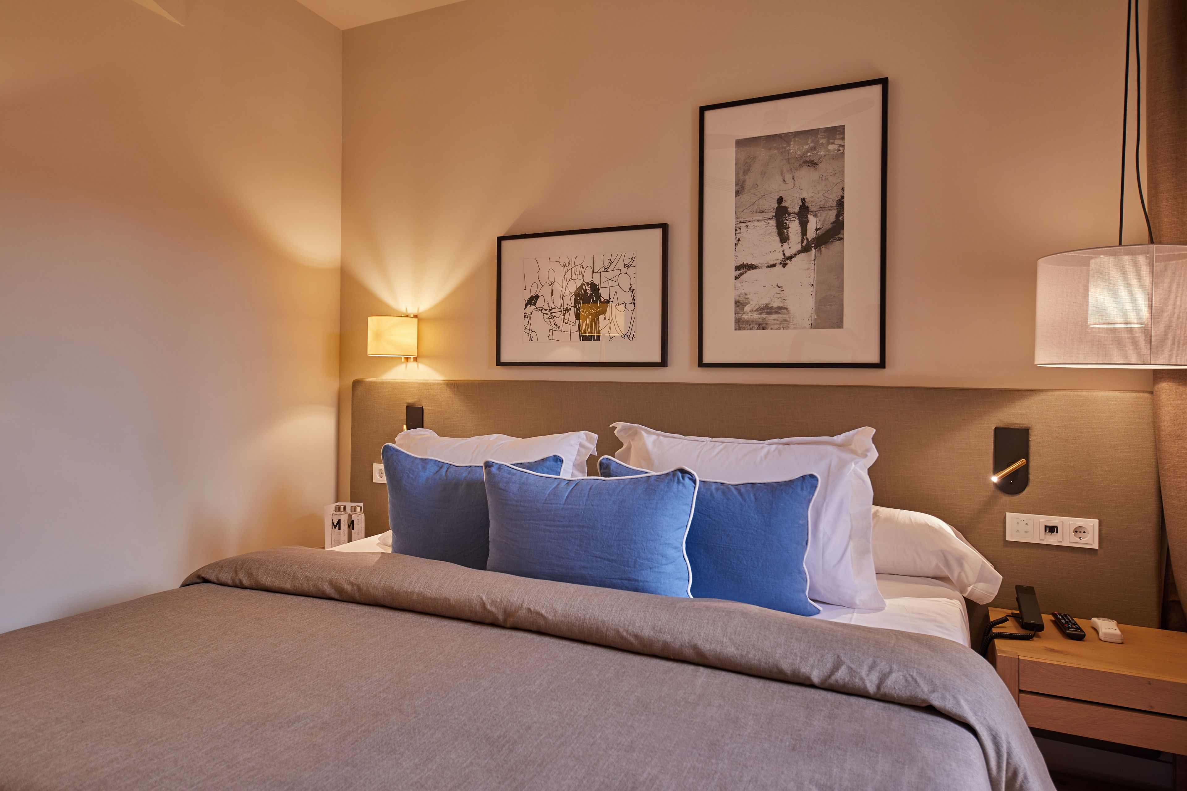 A neatly made bed with blue and white pillows, a bedside table with a lamp, and two framed pictures on the wall.
