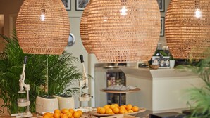 A wooden table with oranges and various food items, surrounded by wicker lamps and potted plants. - Mon Boutique Hotel (Pollenca)