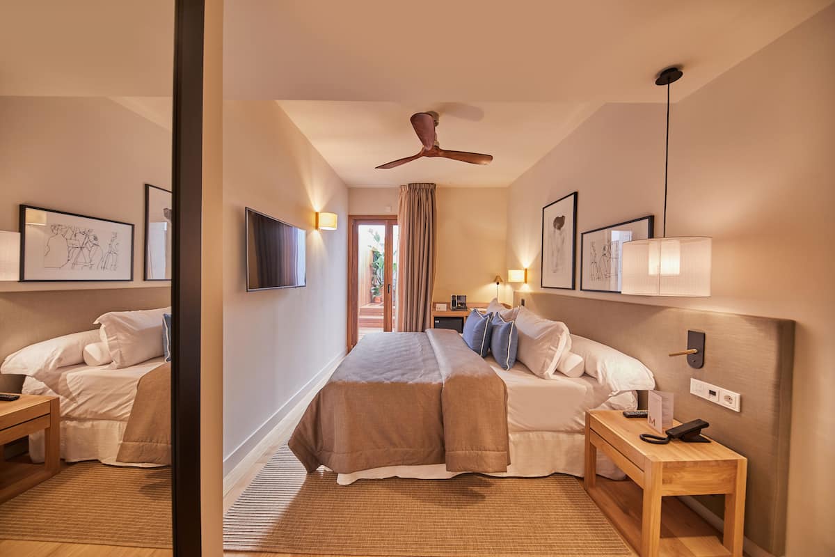 A hotel room with a large bed, two bedside tables, a ceiling fan, and wall-mounted lights.