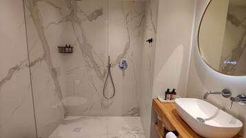 Un baño moderno con pared de ducha de mármol, una bañera independiente y un tocador de madera con lavamanos.