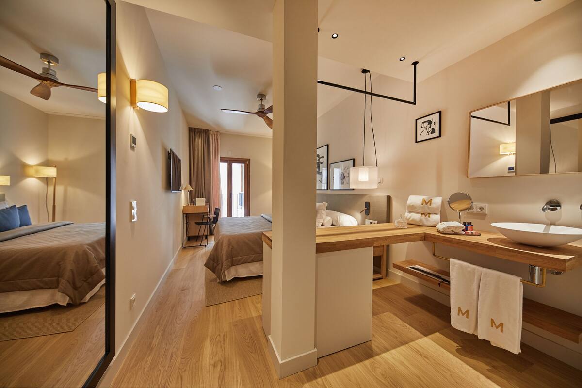 A modern hotel room with a bed, bedside table, and a bathroom with a sink and mirror.