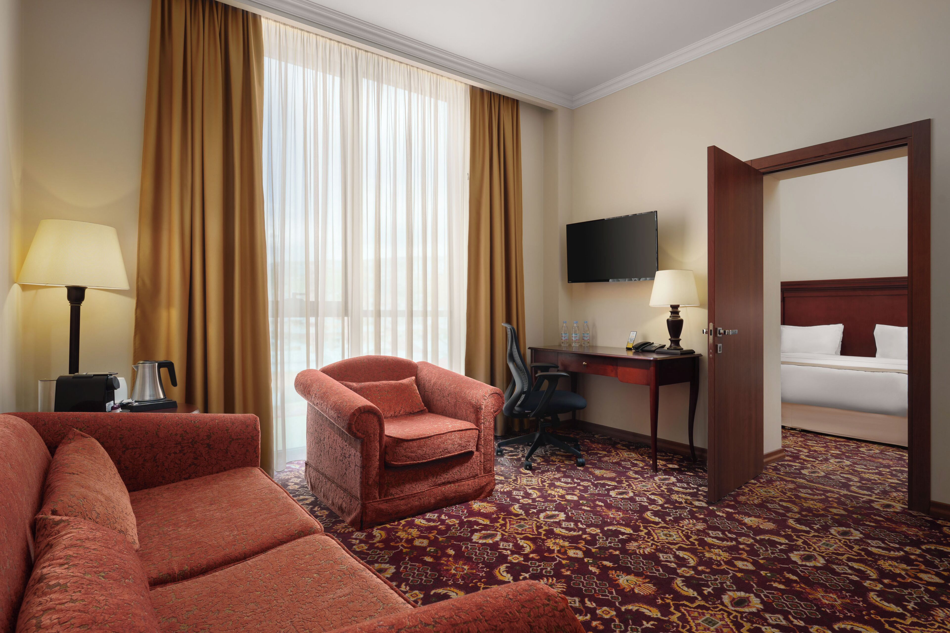 A hotel room with a sofa, armchair, desk, TV, and a bed.