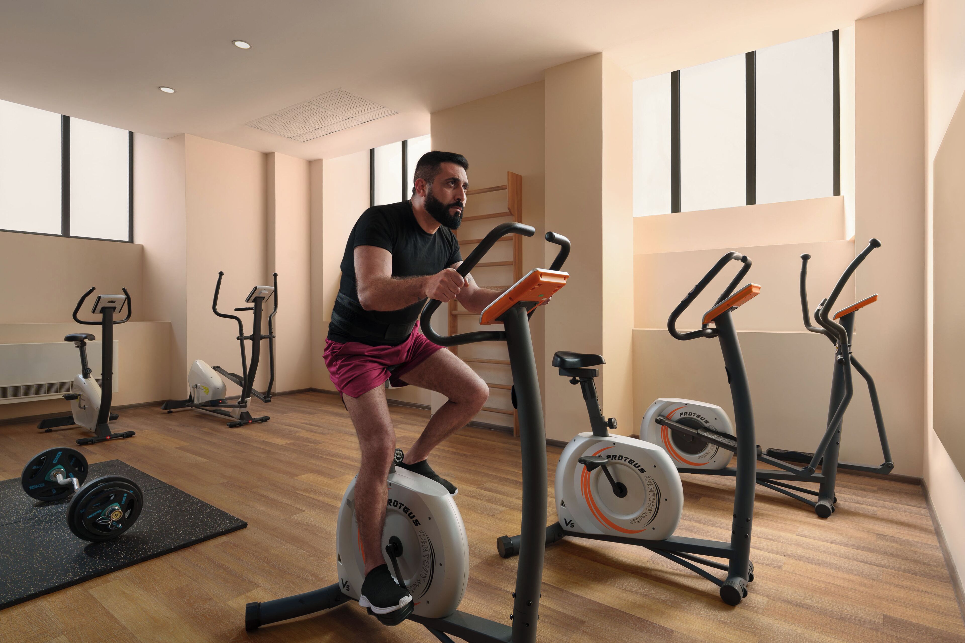 A gym with cardio equipment, a weight bench, and a windowed wall.