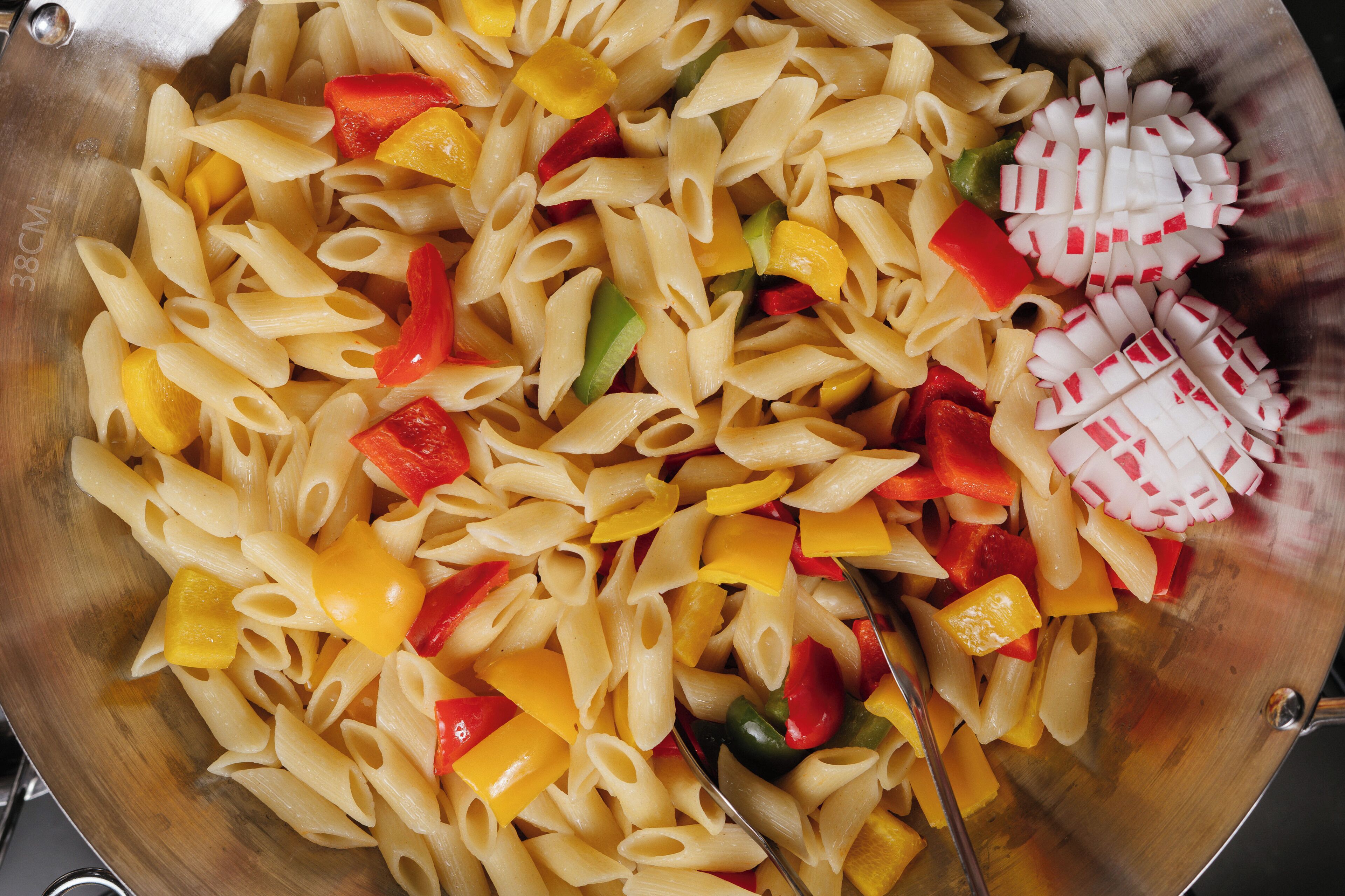 A stainless steel bowl filled with pasta and diced vegetables.