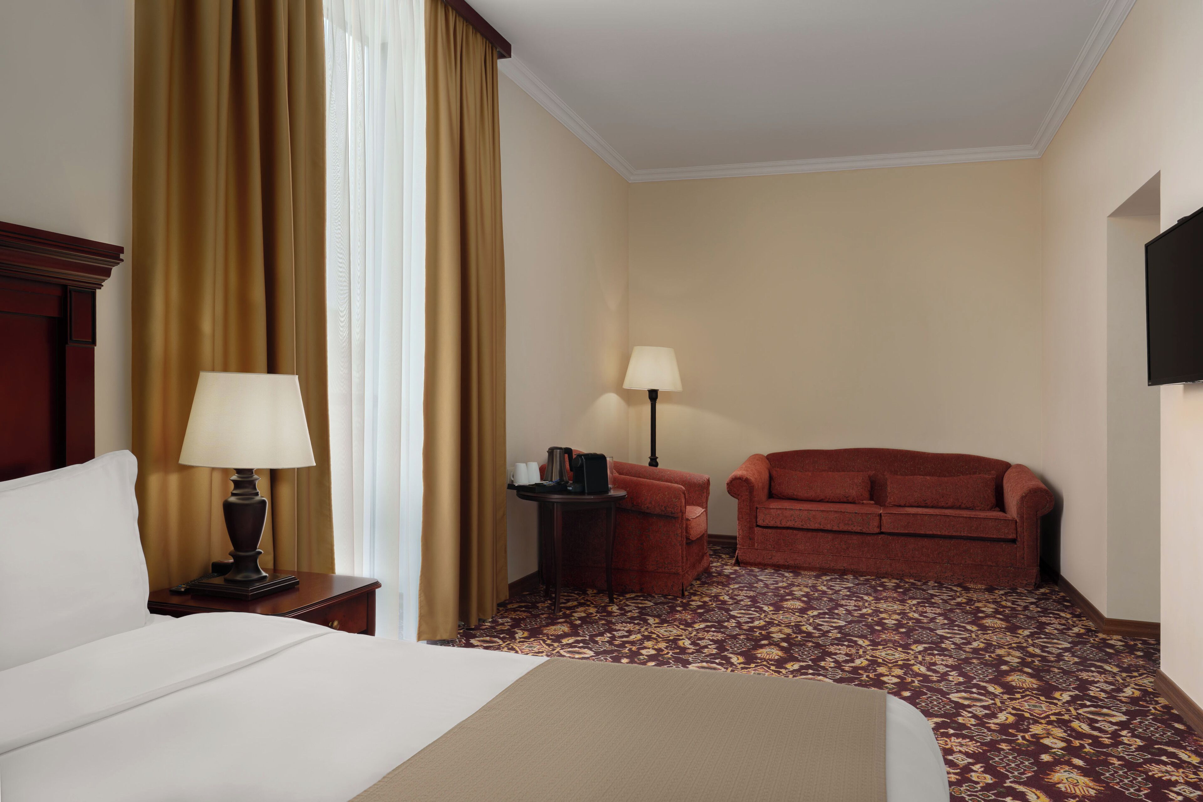 A hotel room with a bed, two lamps, a red sofa, a small table, and a television.