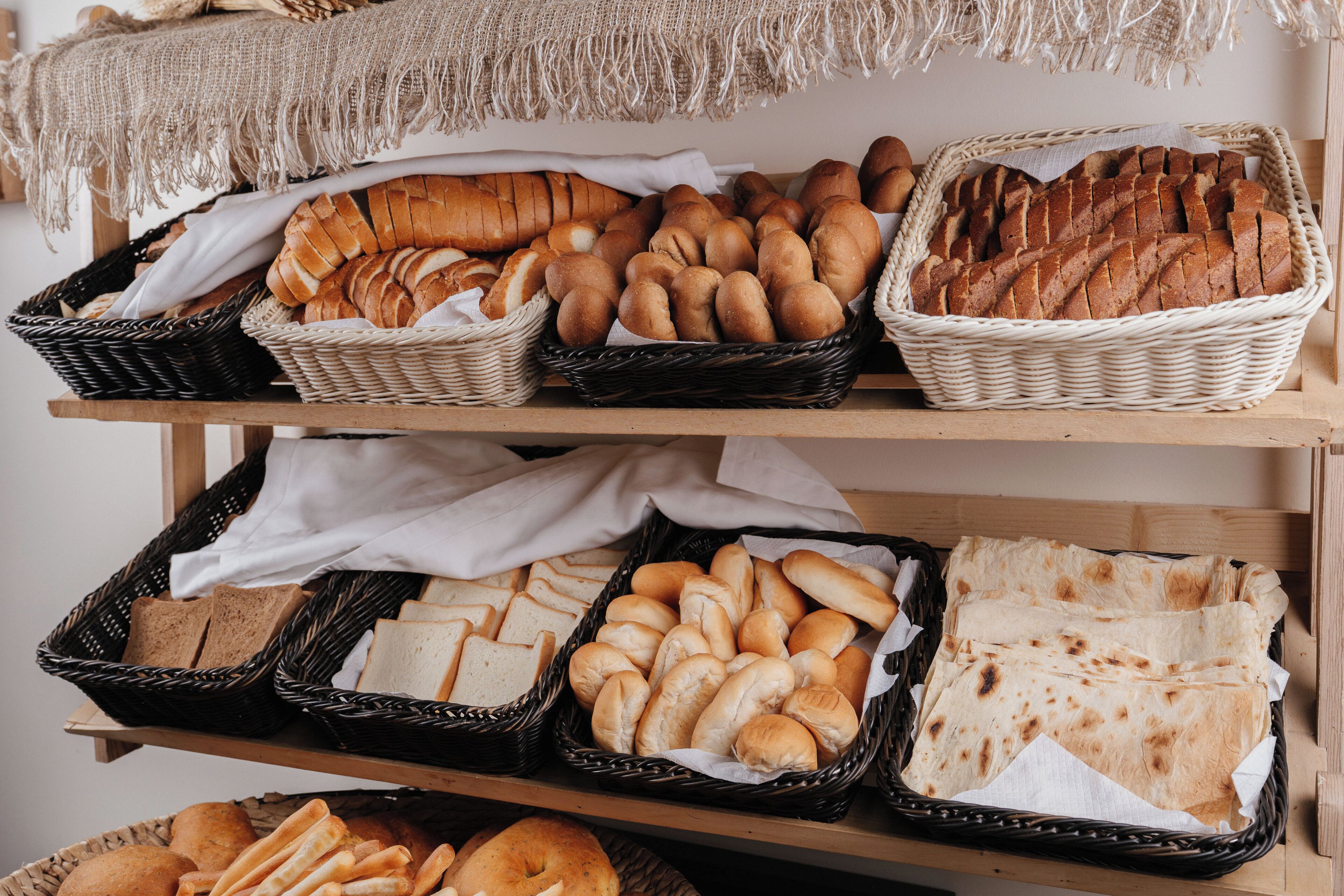 Una variedad de panes y pasteles expuestos en cestas de mimbre sobre estantes.
