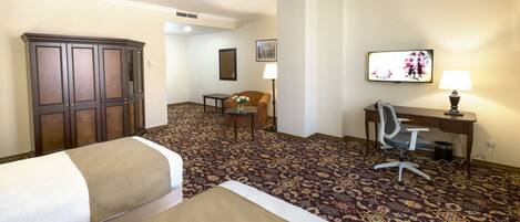A hotel room with two beds, a desk, a chair, a lamp, and a television.