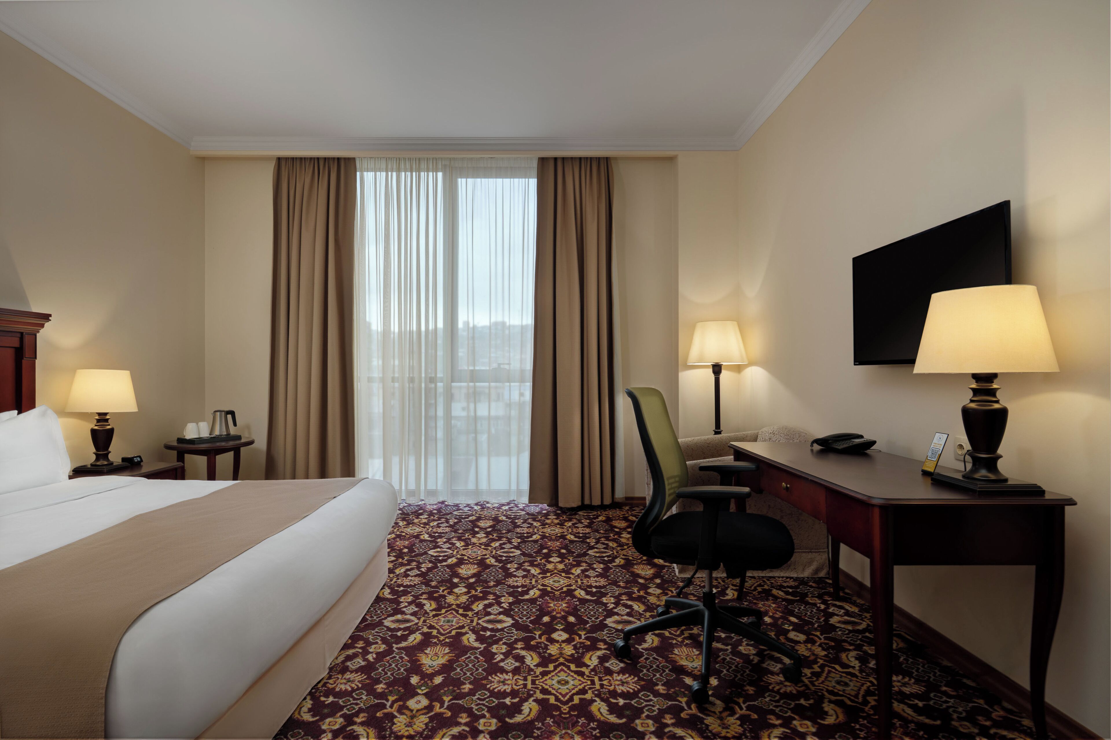 Habitación de hotel con cama, escritorio, silla, lámparas y televisión en la pared.