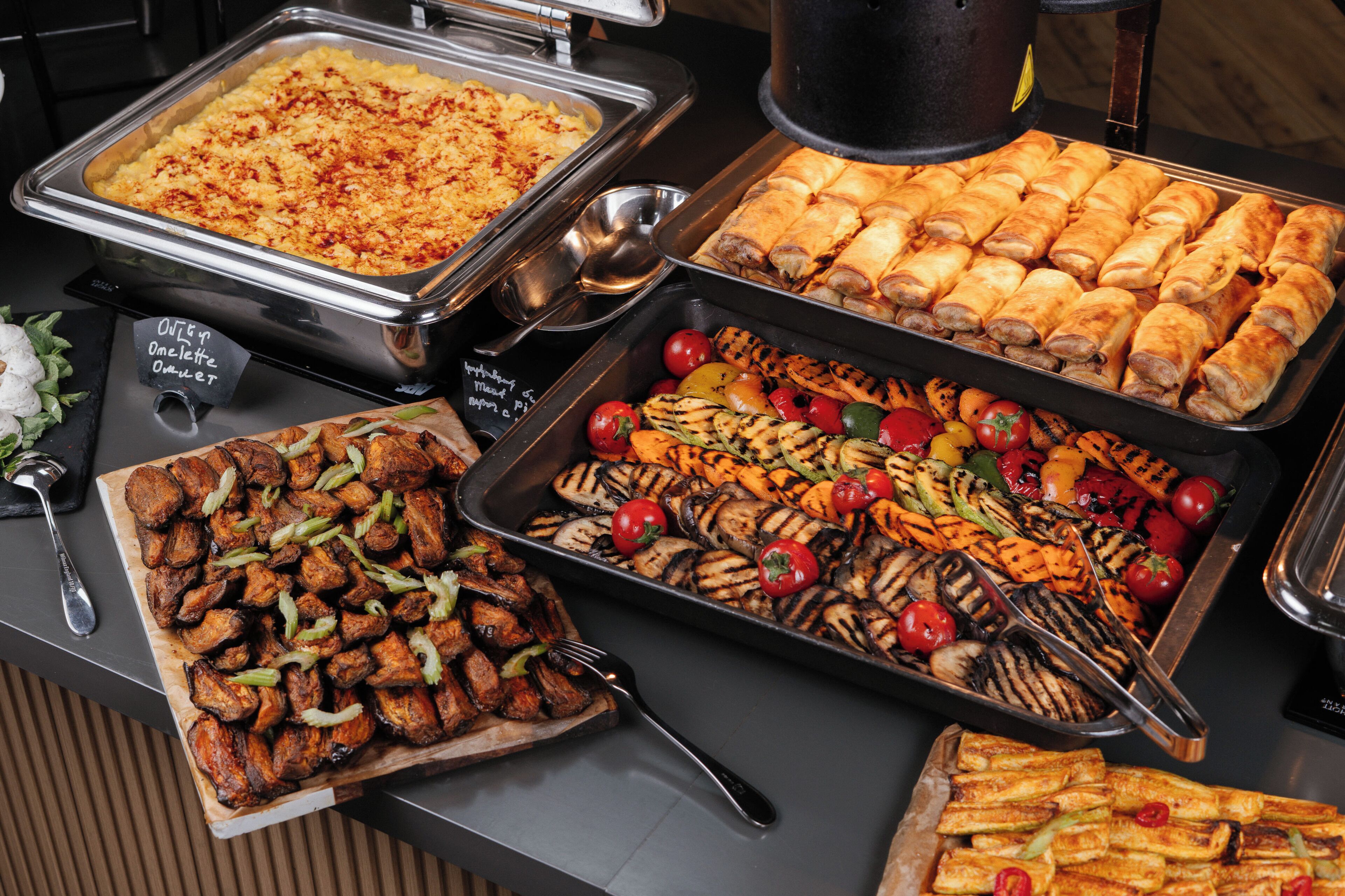 A buffet with various food options including grilled vegetables, meat, and baked goods.