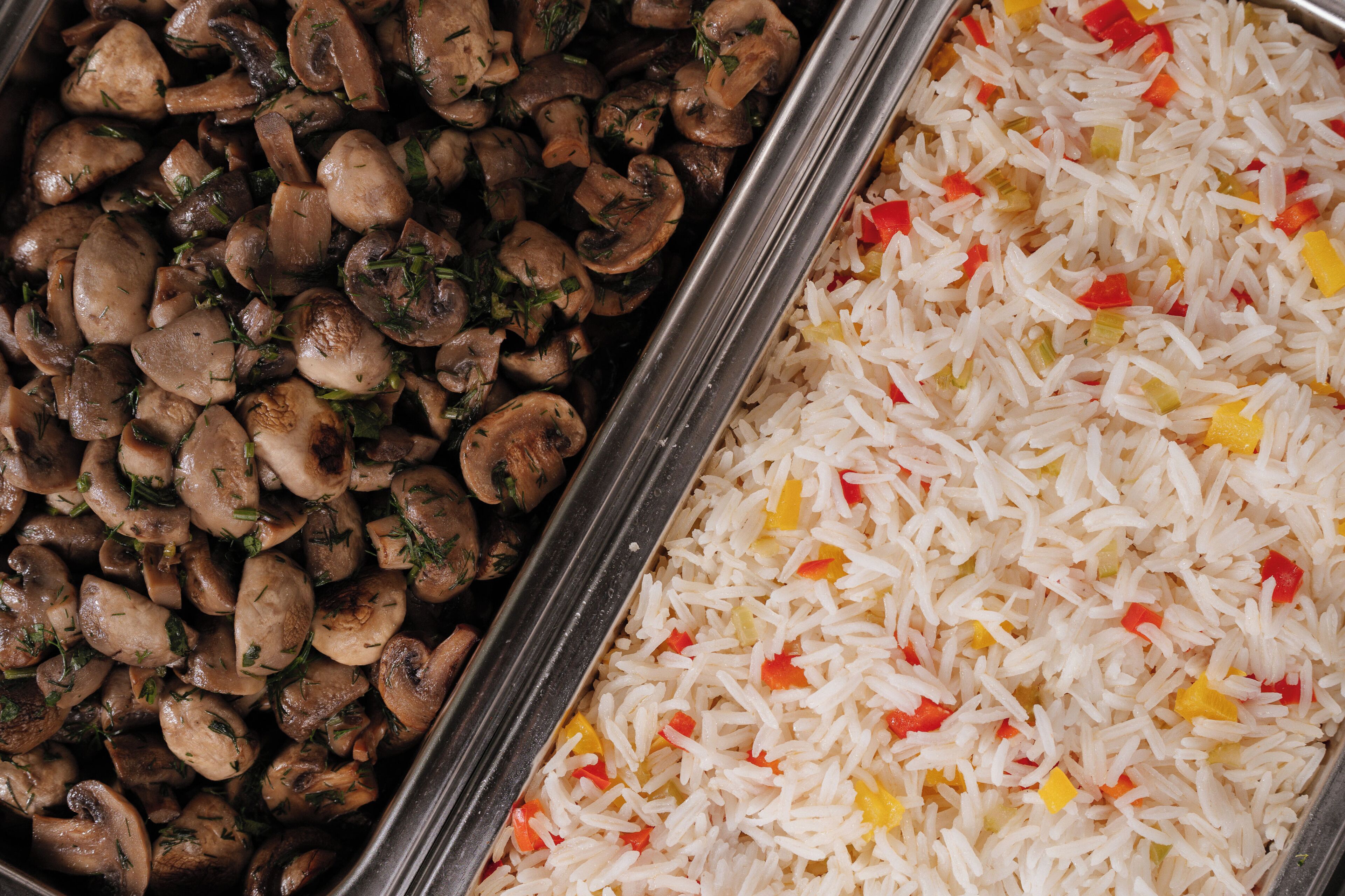 A buffet with two dishes: one of sautéed mushrooms and another of rice mixed with diced vegetables.