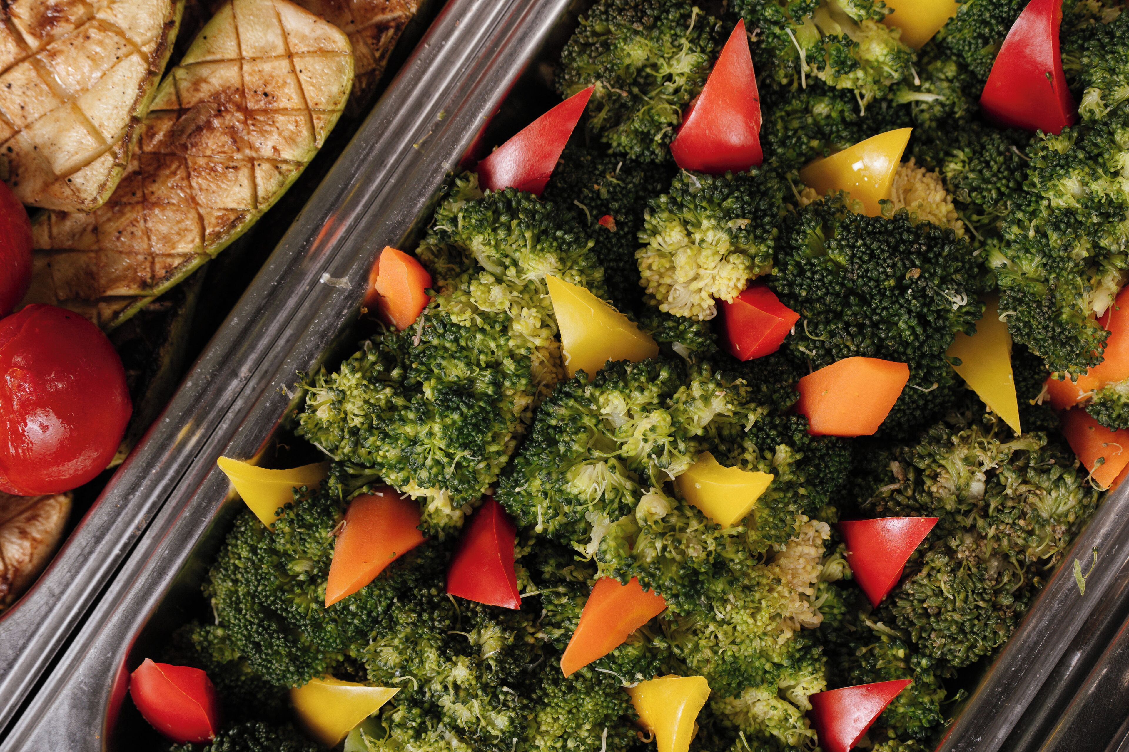 Een schaal met geroosterde groenten, waaronder broccoli, wortelen en tomaten.