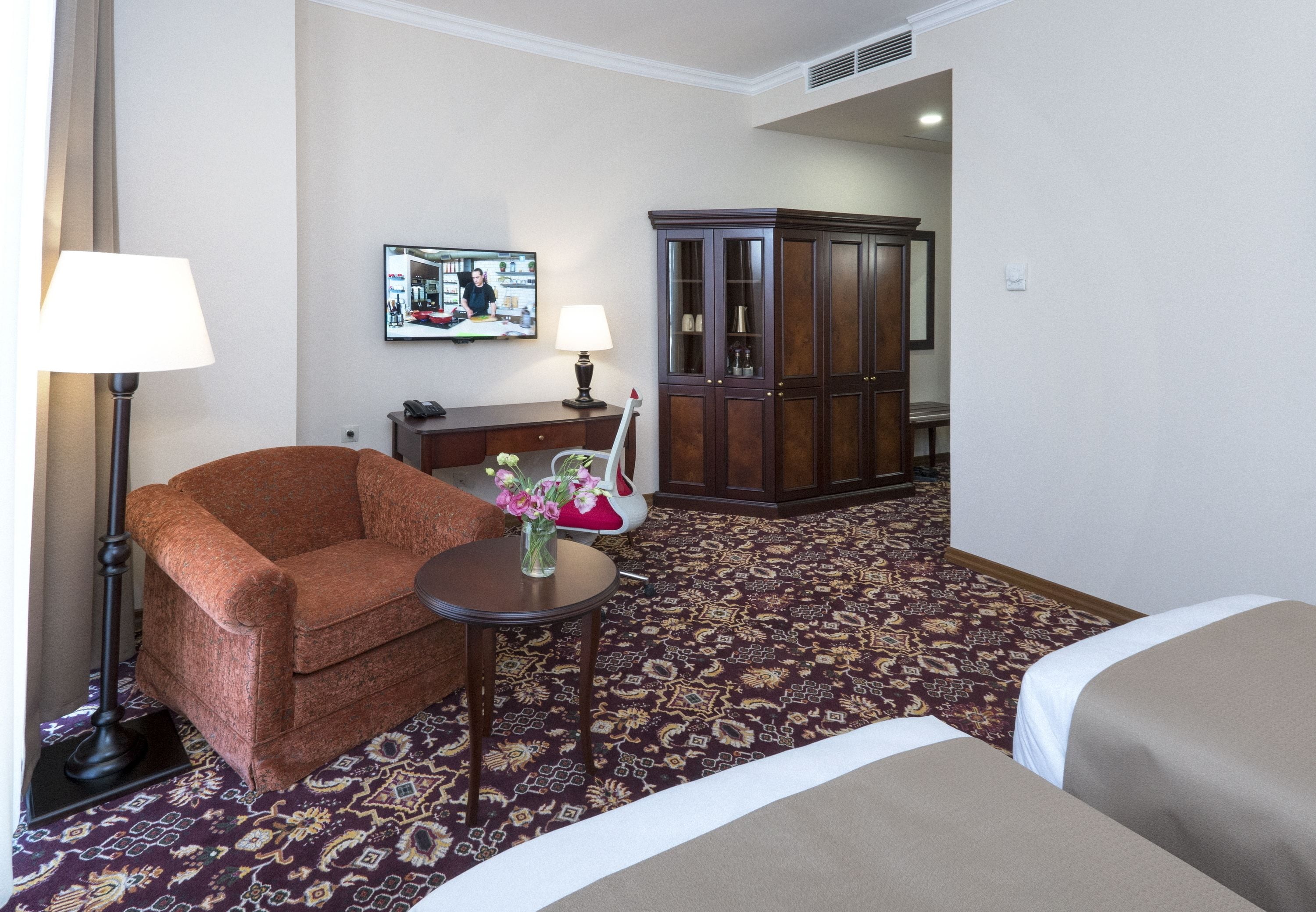 A hotel room with a sofa, a small table with a vase of flowers, a cabinet, and a bed.