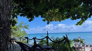 Eine Holzterrasse mit Seilzaun, mit Blick auf ein ruhiges Meer mit Booten und einem klaren Himmel.