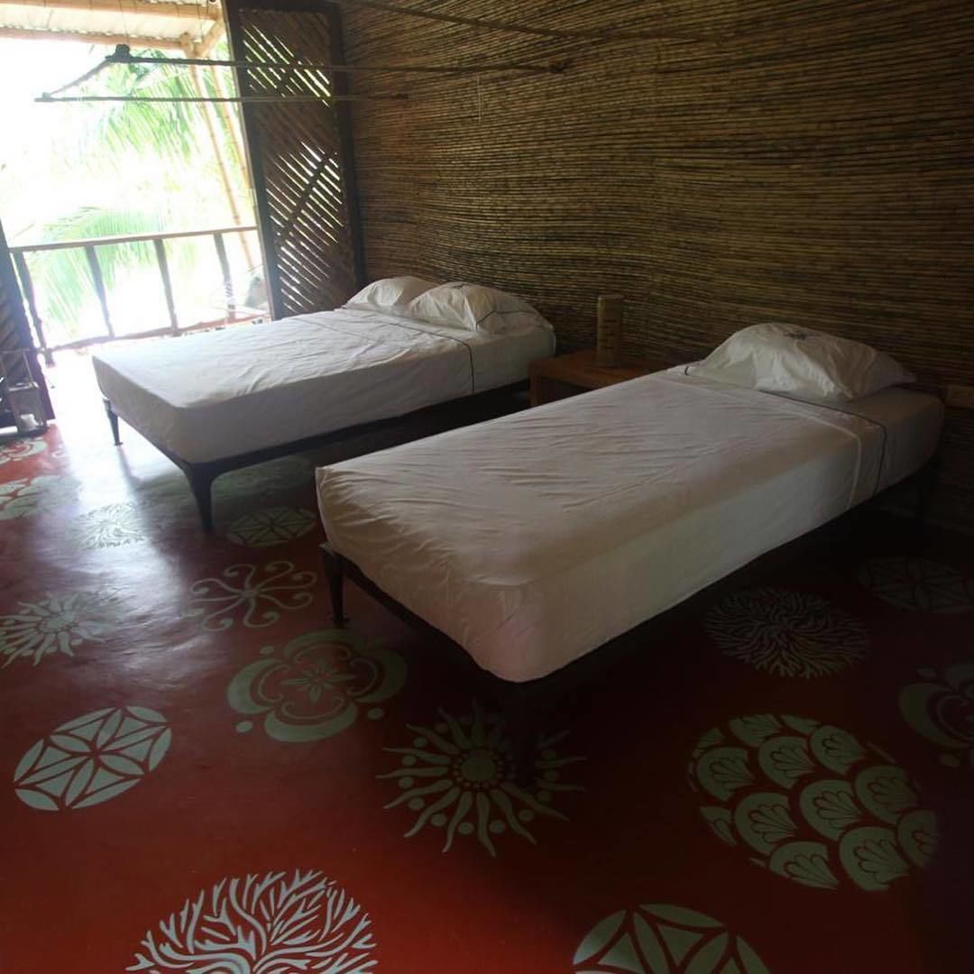 A room with two single beds, a patterned floor, and a bamboo wall.