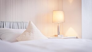 A neatly made bed with white bedding and pillows, a bedside table with a lamp, and a wall with vertical lines. - Hotel Spies (Gladenbach)