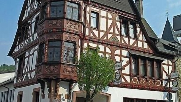 A traditional half-timbered building with a steeply pitched roof, a visible chimney, and a small tree in front. - Hotel Spies (Gladenbach)