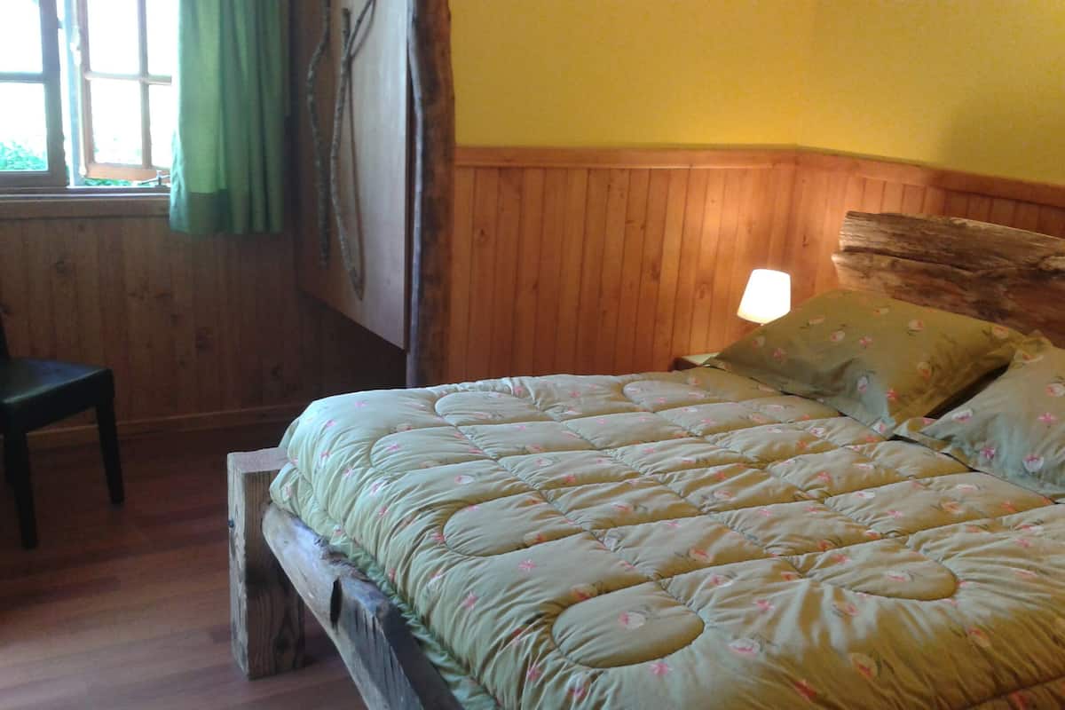A wooden bed with a quilted green blanket, a wooden headboard, and a single bedside lamp.
