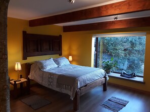 A bedroom with a wooden bed, two bedside lamps, a patterned rug, and a window with a view of greenery.
