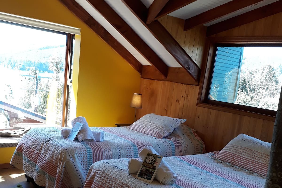 A cozy room with two beds, wooden beams on the ceiling, and large windows.