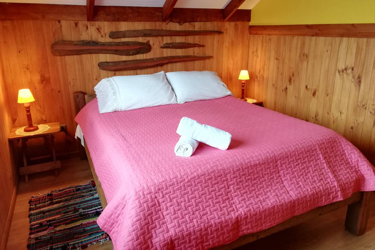 A wooden-paneled room with a bed, two bedside lamps, and a wooden bench.