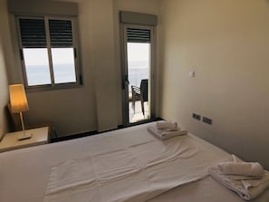 Habitación de hotel con cama, escritorio con lámpara, silla y puerta al balcón.
