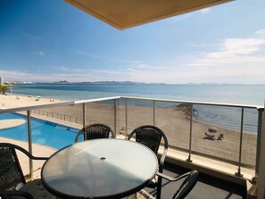 Un balcón con piscina, vista al mar y mobiliario exterior.
