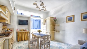 A compact kitchen with a dining area, a sofa, and a TV mounted on the wall. - Alpa Suite (Sant'Agnello)