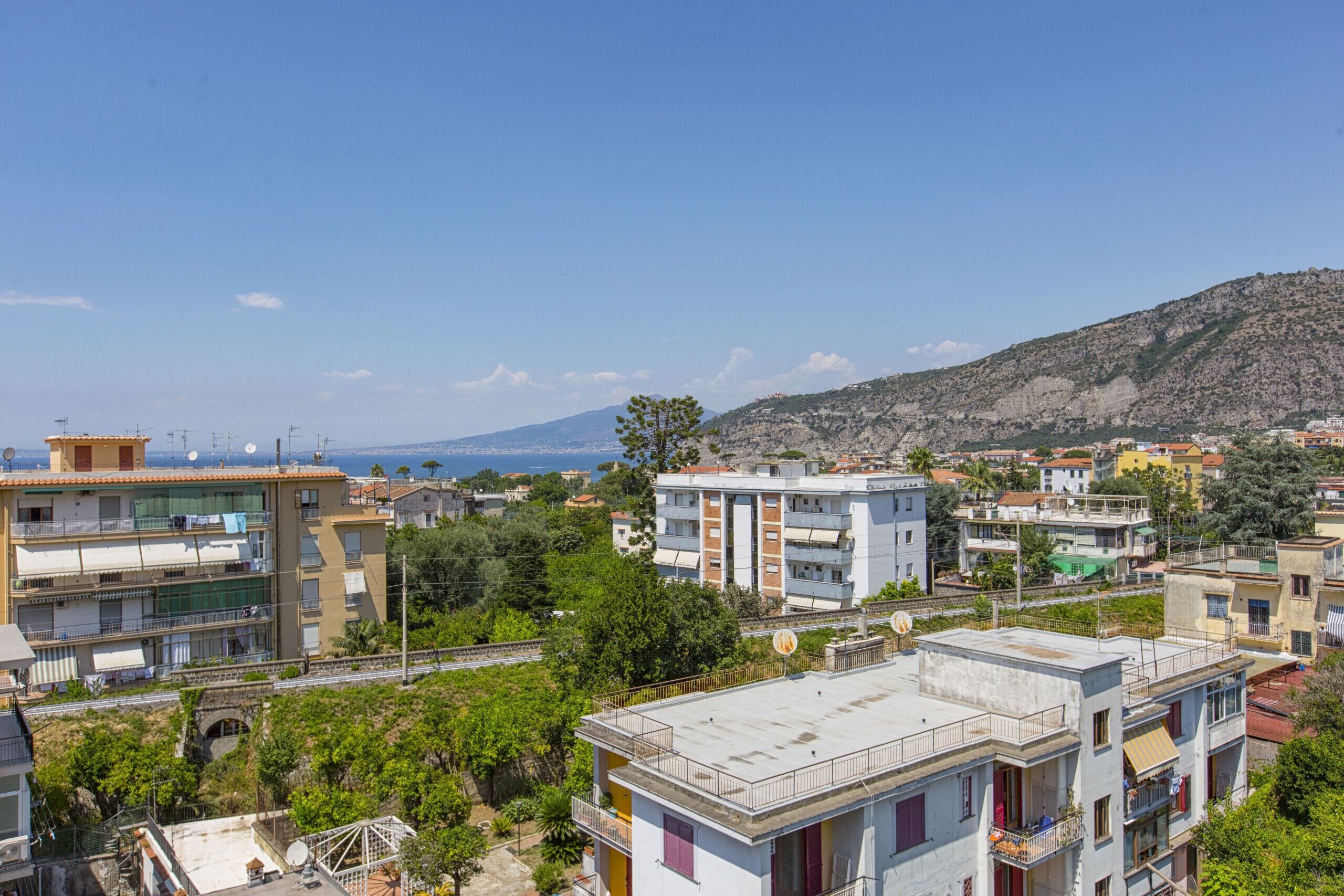 A residential area with multi-story buildings, a mountain in the background, and a clear sky.