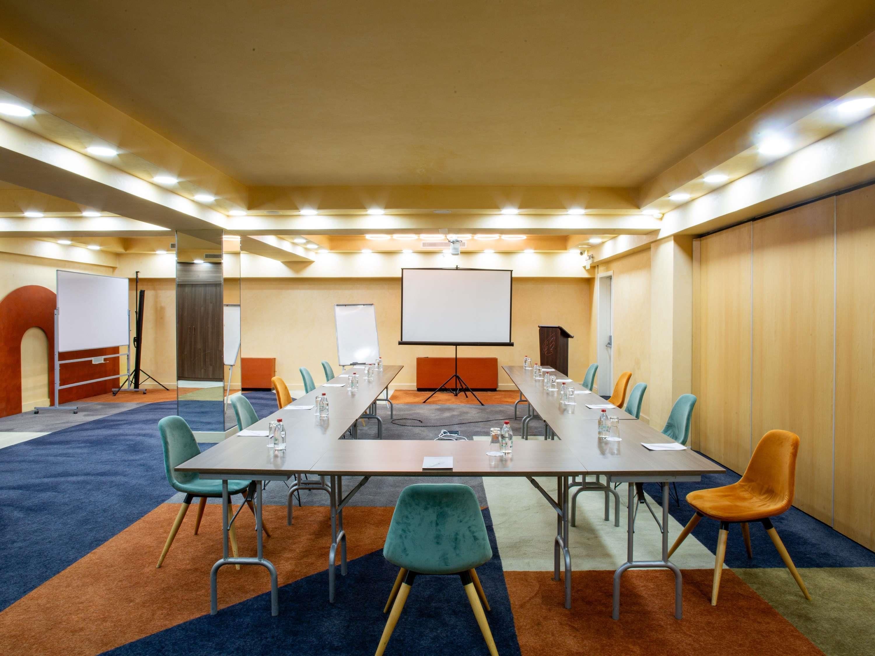 A conference room with a long table, chairs, a whiteboard, and a projector screen.