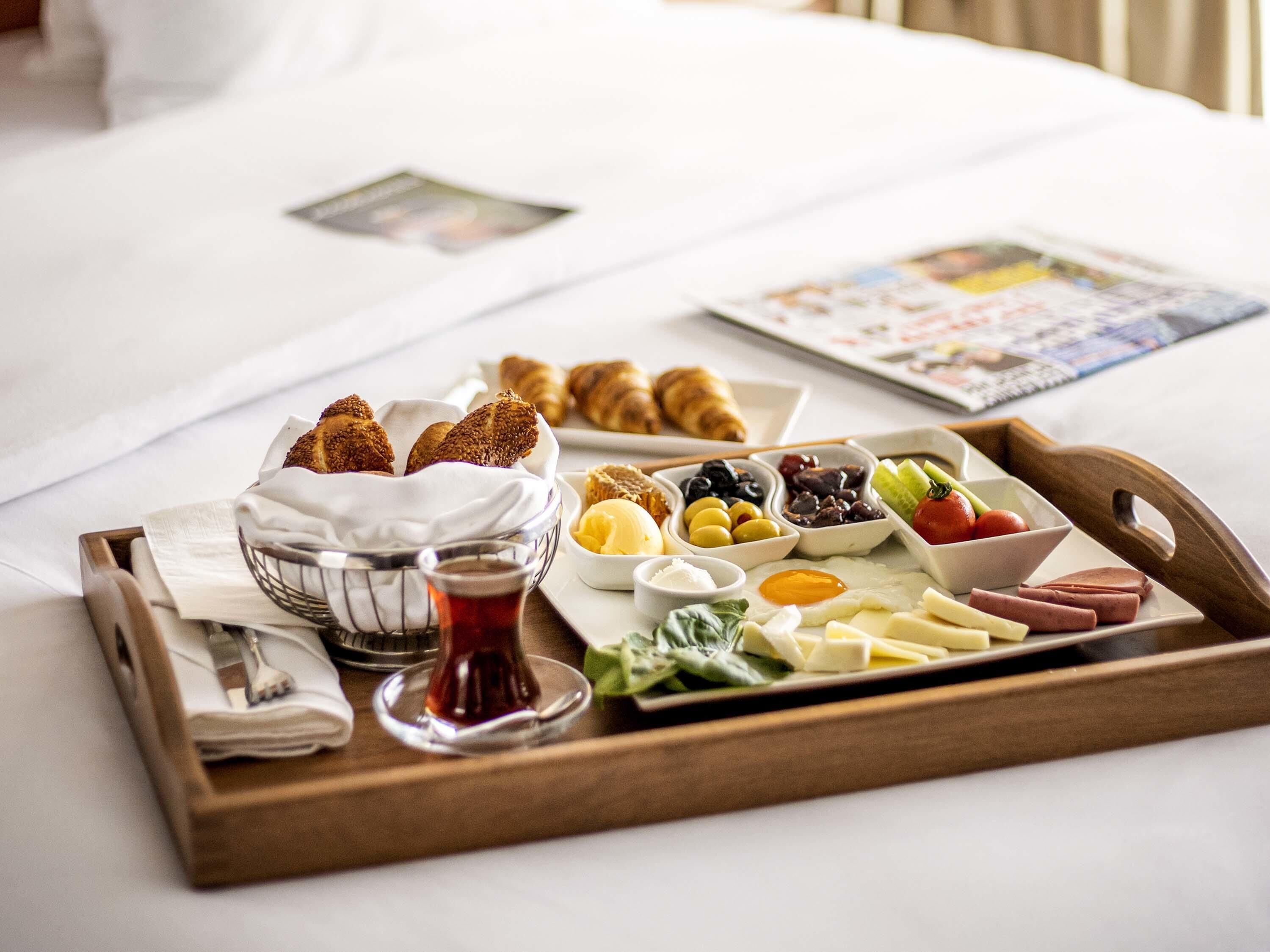 A breakfast tray with croissants, cheese, eggs, and various fruits on a bed.