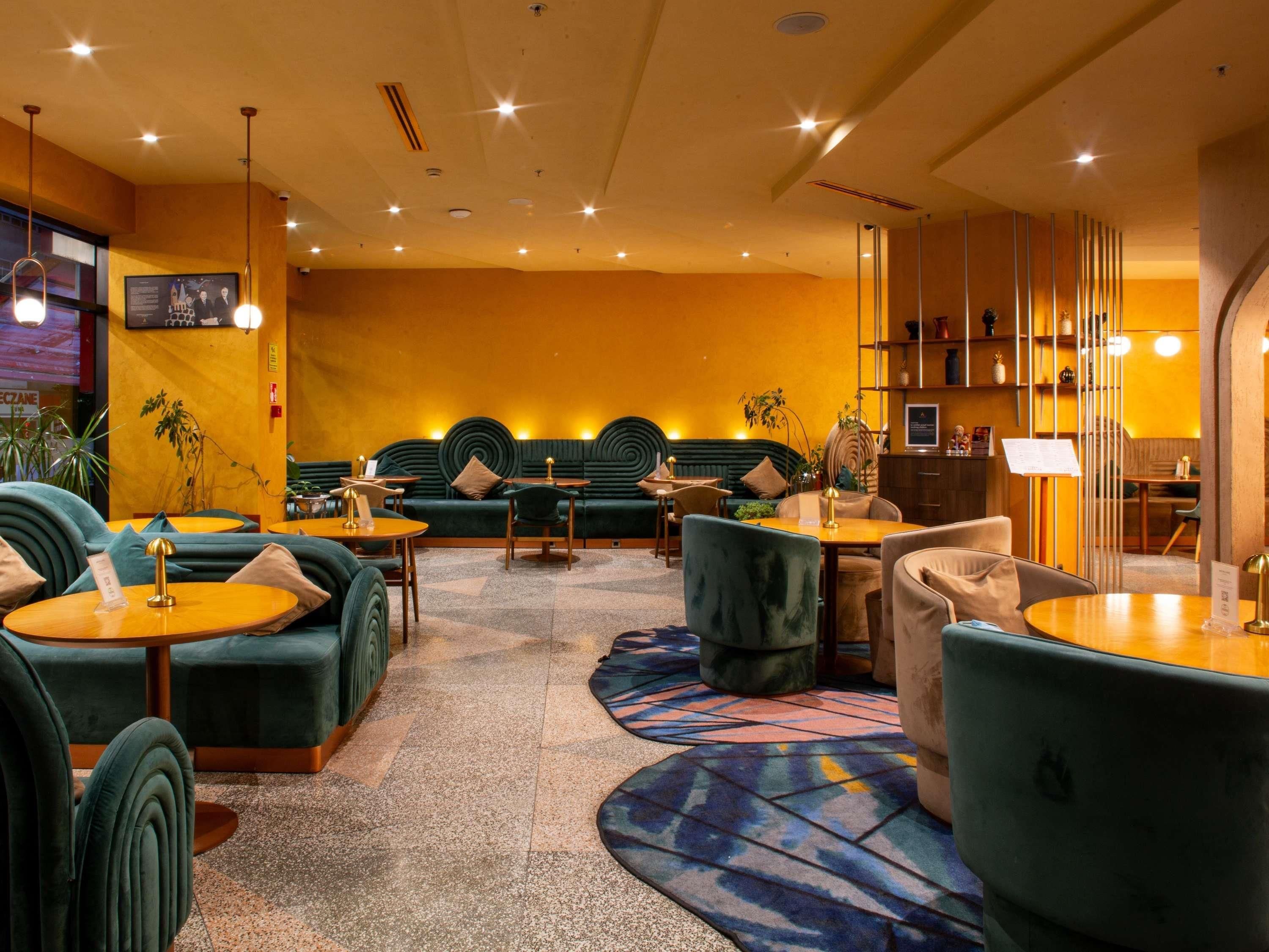 Un hall d’hôtel avec des canapés verts, des tables en bois et un tapis à motifs.
