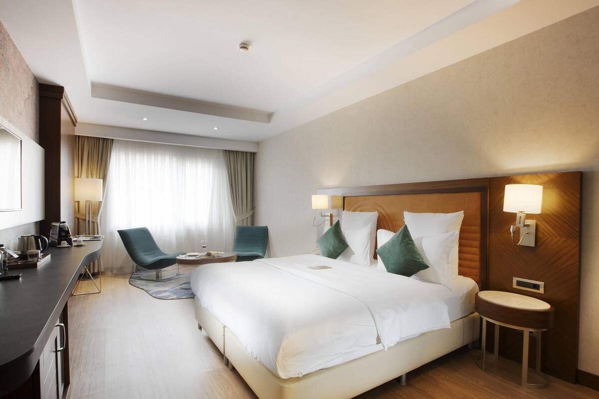 Ein Hotelzimmer mit einem Bett, zwei Stühlen, einem Schreibtisch, einer Lampe und einem Nachttisch.