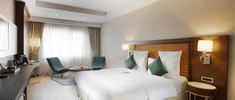 A hotel room with a bed, two chairs, a desk, a lamp, and a bedside table.