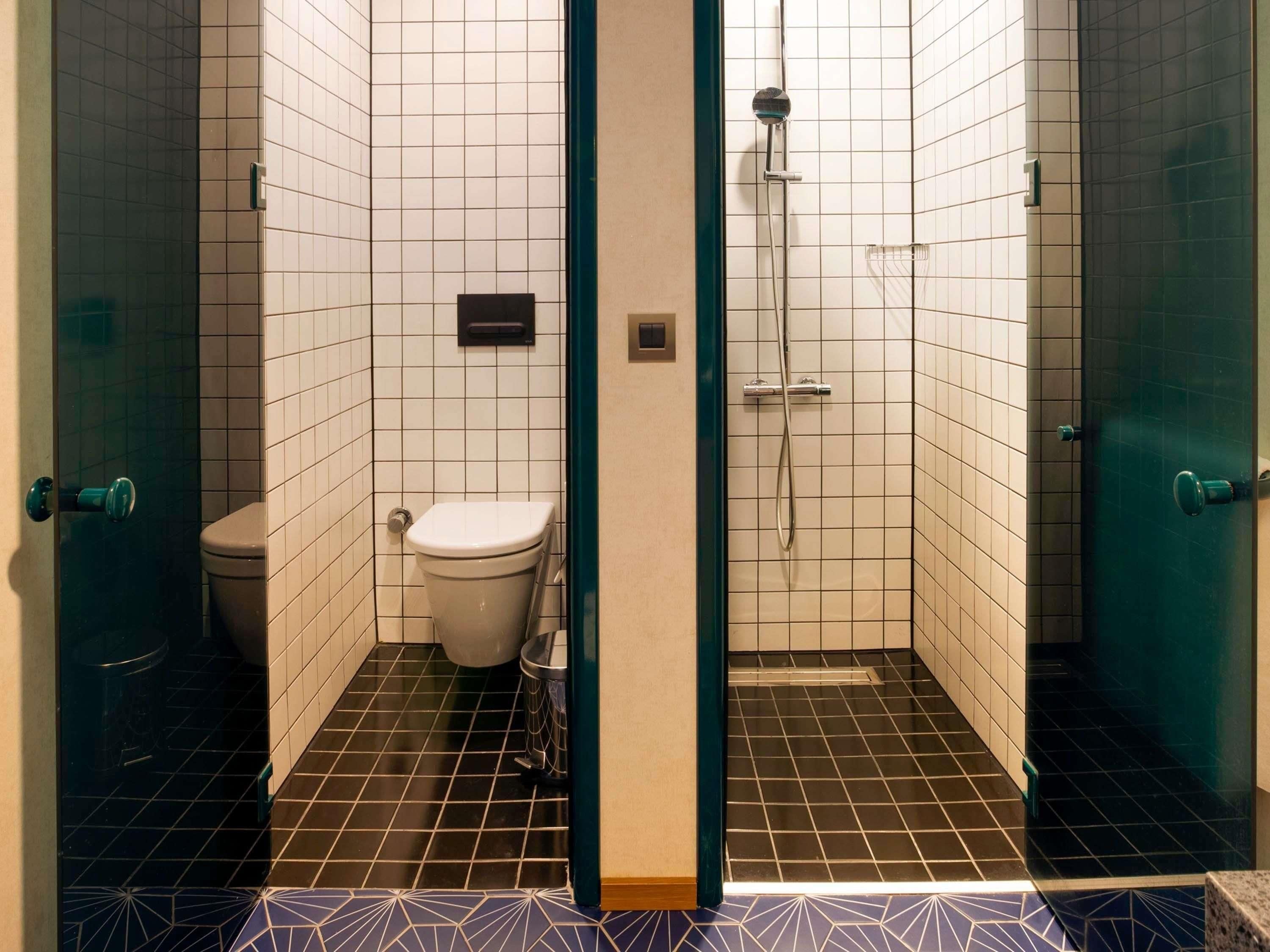 Pieni, laatoitettu kylpyhuone, jossa on wc, suihku ja roskakori.