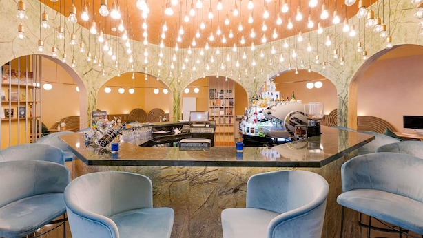A bar area with a marble floor, blue cushioned seating, and a bar counter with a cash register and various bottles. - Mercure Istanbul Bakirkoy (Istanbul)
