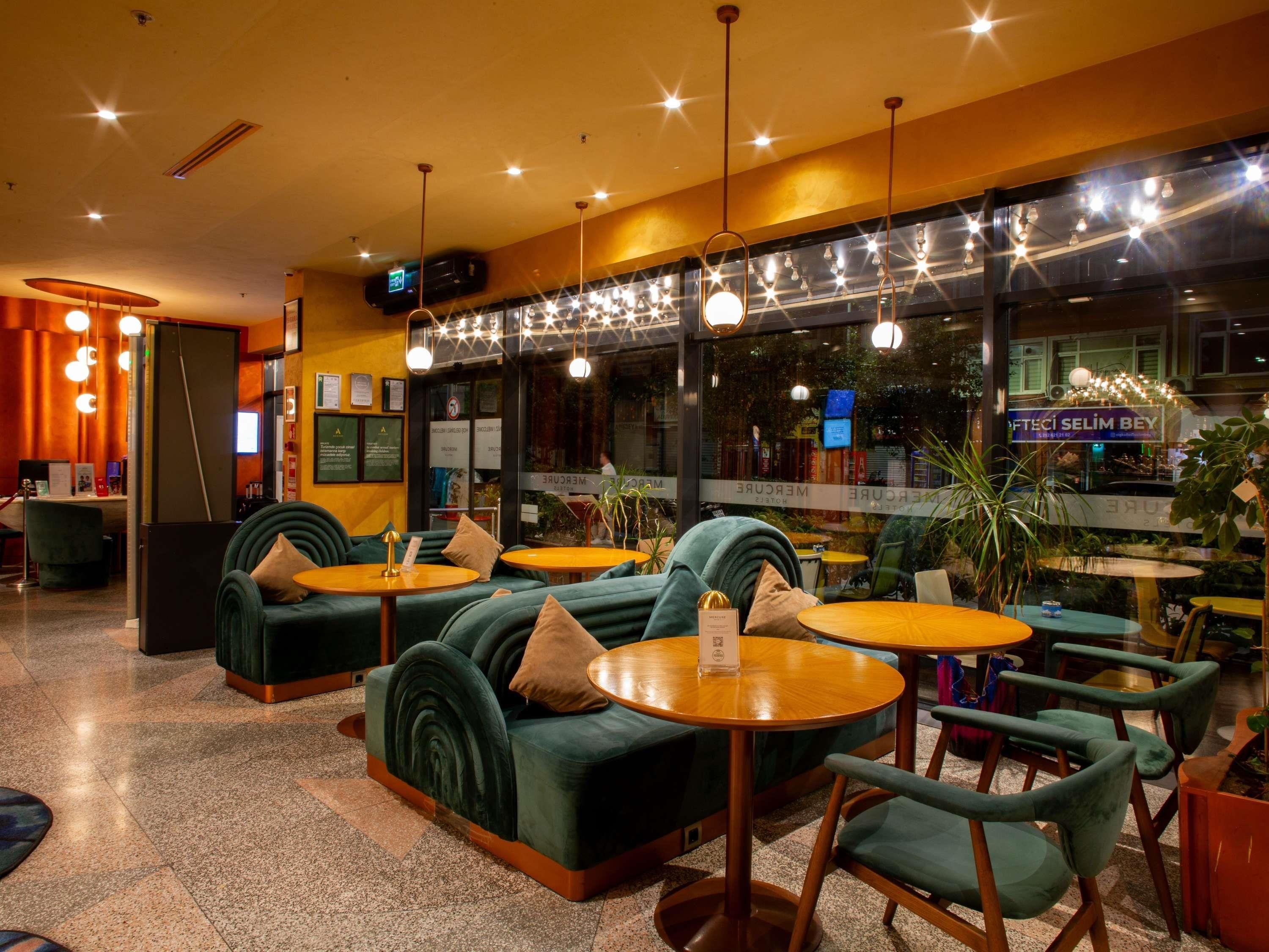 A hotel lobby with green sofas, wooden tables, and pendant lighting.