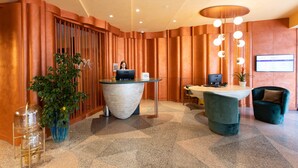 A modern reception area with a curved reception desk, a seating area with a green chair, and a potted plant. - Mercure Istanbul Bakirkoy (Istanbul)
