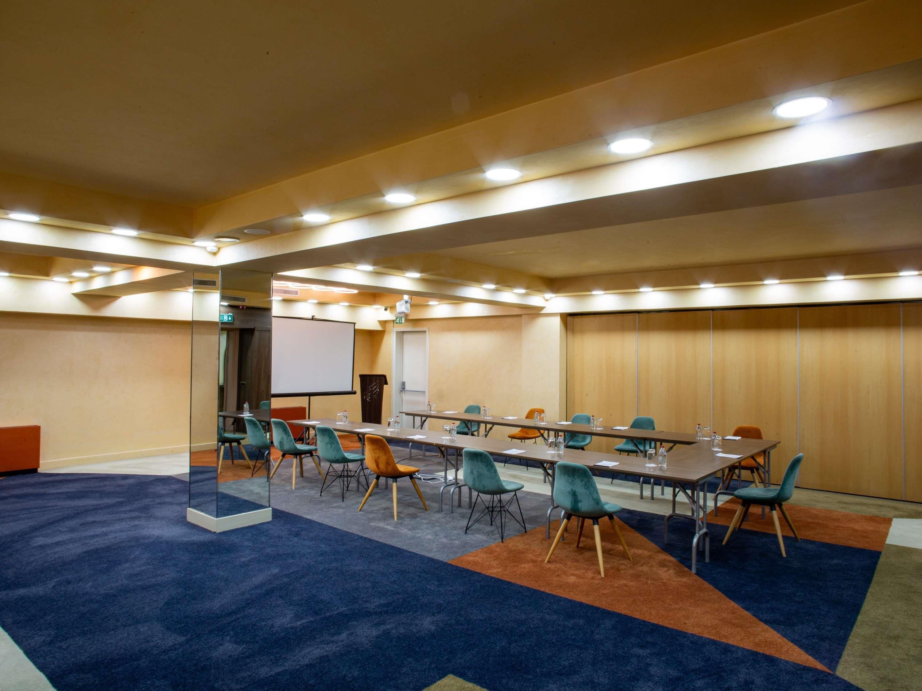 A conference room with a long table, multiple chairs, a projector screen, and carpeted flooring.