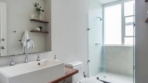 A modern bathroom with a large white sink, a glass shower enclosure, and wooden shelves with decorative items. - Top Location Polanco by Mr.W (Mexico City)